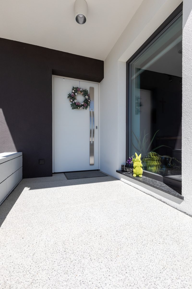 White front door with a narrow glass strip and a wreath at a modern entrance