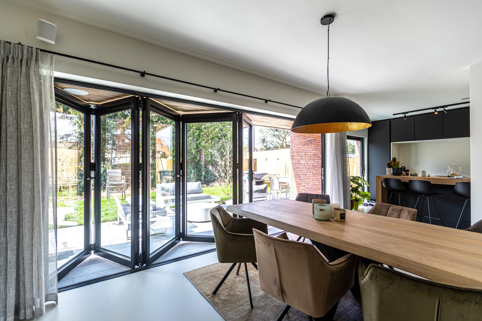 Black folding doors opening a dining room onto a garden