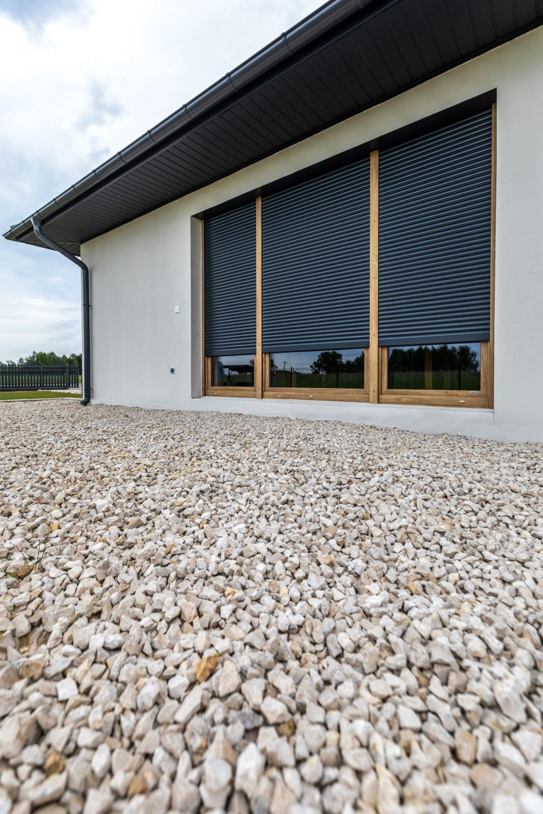 Dark roller shutters half lowered over large timber-effect windows
