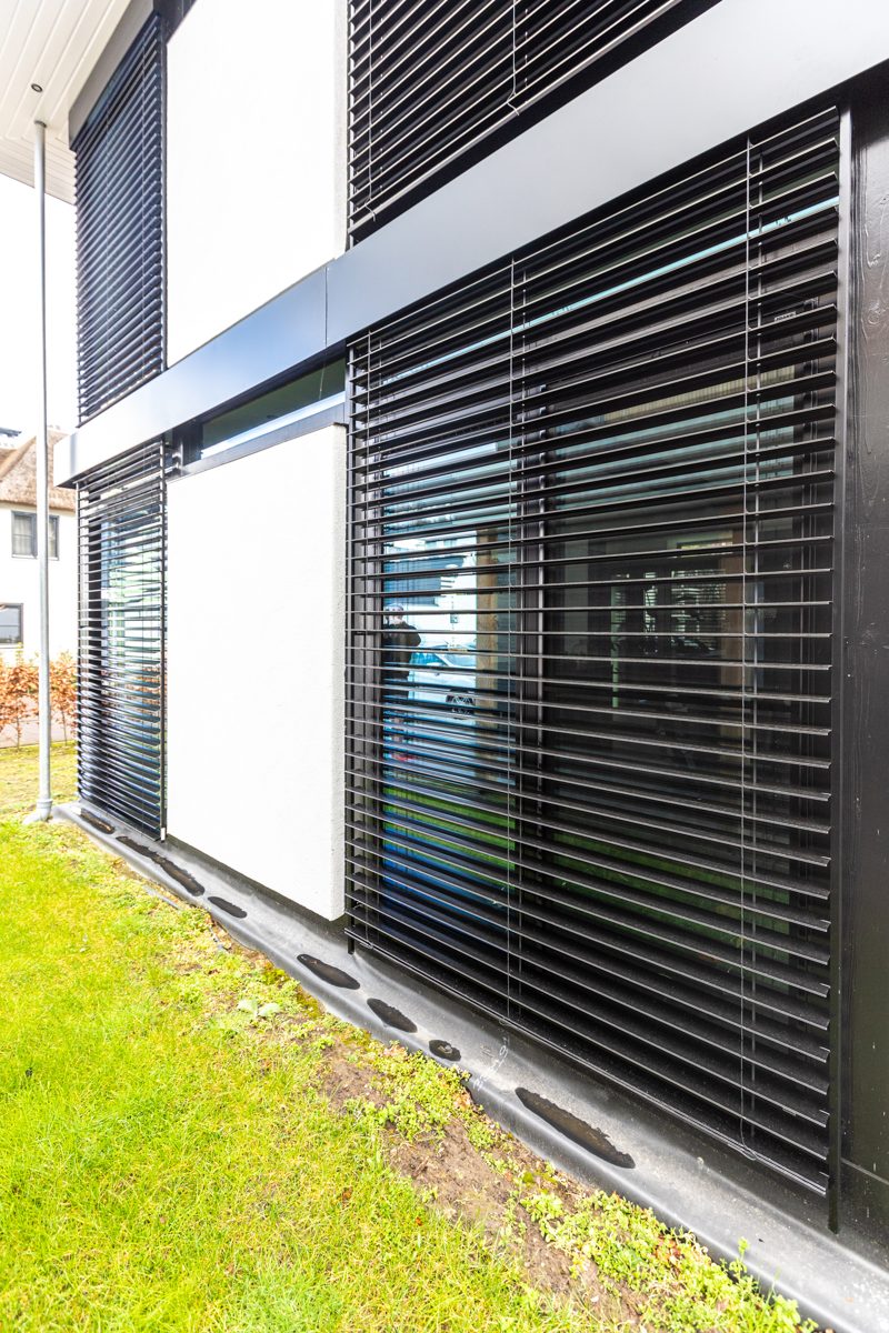 Large black venetian blinds over tall glazing on a corner of the house
